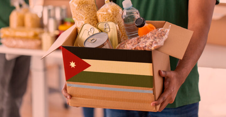 male volunteer's hands holding box with food over group of people at distribution or refugee assistance center
